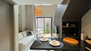 A modern living room with a sofa, dining table, and kitchen area. - Smeralda del Mare Residence - Porto de Galinhas (Ipojuca)