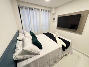 Ein Schlafzimmer mit einem Bett, Kissen, einem Fernseher und einem Fenster mit Vorhängen.