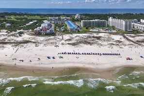 Vista aérea de un complejo turístico en la playa con varias edificaciones, una playa de arena y olas del océano.