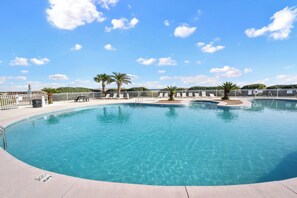 Una piscina azul cristalina con palmeras, una cerca blanca y un cielo despejado.