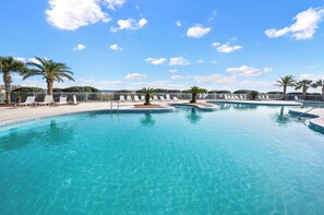 Ein großer, klarer Swimmingpool mit mehreren Liegestühlen und Palmen, umgeben von einem weißen Zaun.