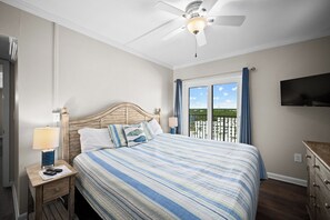 A bedroom with a bed, nightstands, a desk, a ceiling fan, and a TV mounted on the wall.