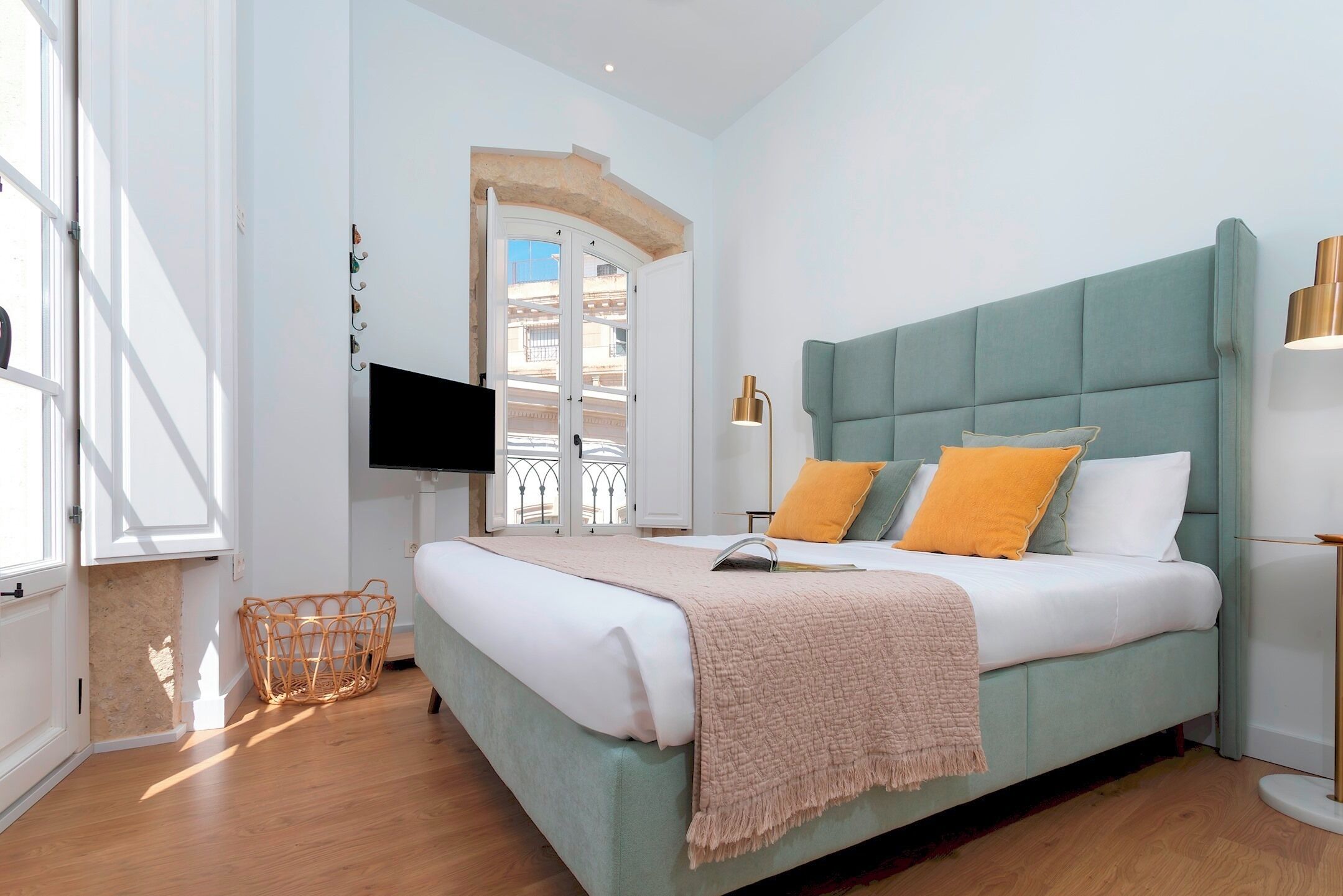 Un dormitorio moderno con una cama grande, un televisor montado en la pared y una ventana con vistas a edificios.