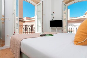 Quarto com cama, TV fixada na parede e varanda com vista para edifícios.
