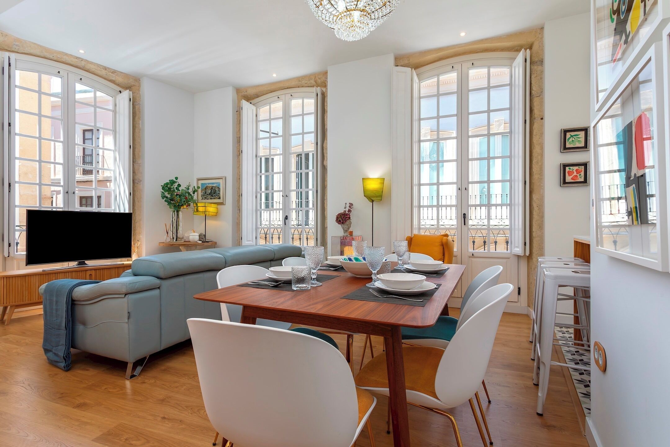 A modern living space with a dining area, a sofa, a television, and large windows.