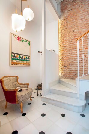 A room with a red upholstered armchair, a white staircase, and a brick wall. - Genteel Home Casa de los 12 Balcones (Almeria)