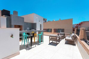 Terraço no telhado com área de estar ao ar livre, um bar e vista dos edifícios circundantes.