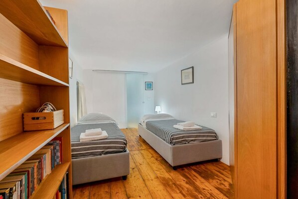 A compact room with two beds, wooden flooring, a bookshelf, and a door. - [Al Castello] 5Terre-Near the station+A/C (La Spezia)