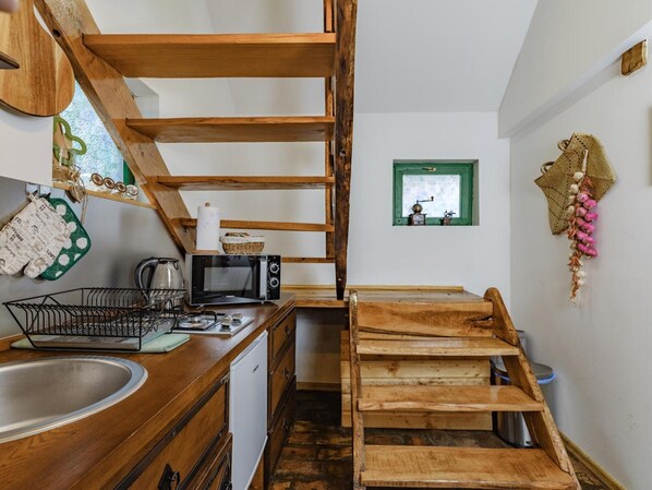 A compact kitchen with wooden shelves, a microwave, a sink, and a small window.