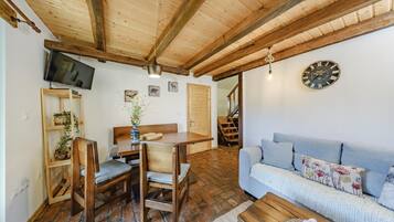 Una sala de estar acogedora con techo de madera, un sofá, una mesa de comedor con sillas, un televisor montado en la pared y un reloj.