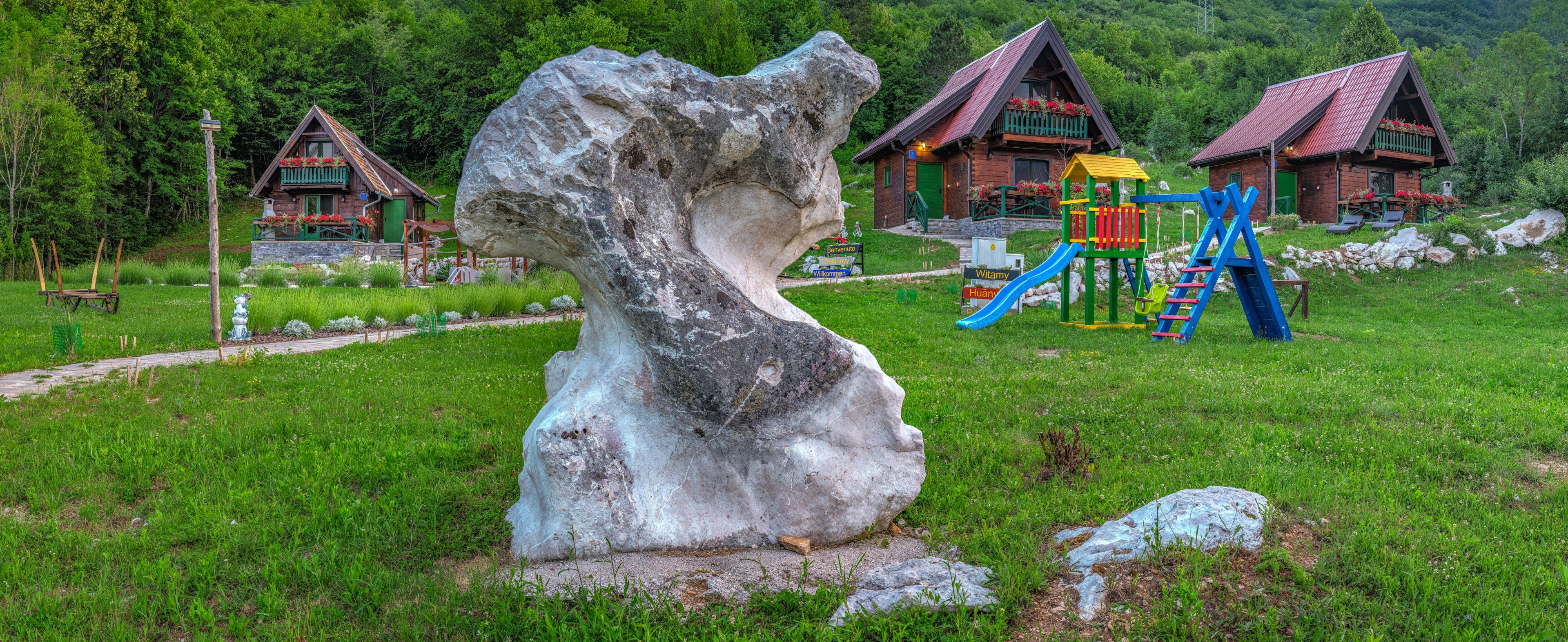 A rustic cabin with a wooden exterior, surrounded by lush greenery and a large rock sculpture.