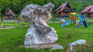 A rustic cabin with a wooden exterior, surrounded by lush greenery and a large rock sculpture.