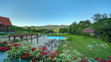 A backyard with a swimming pool, a wooden pergola, and a garden with red flowers.