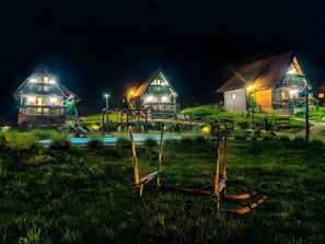Une vue nocturne d’un complexe hôtelier comprenant plusieurs maisons en bois, une piscine et un panneau indiquant « Bienvenue ».