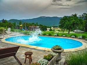 A swimming pool with a water feature, surrounded by a landscaped garden, with mountains in the background.