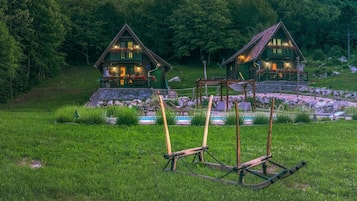 A rustic cabin with a stone foundation, a wooden deck, and a small garden area with a swing set.