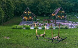 A rustic cabin with a stone foundation, a wooden deck, and a small garden area with a swing set.