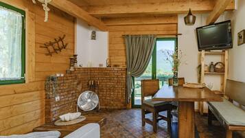 L’intérieur d’un chalet accueillant, avec une cheminée en briques, des meubles en bois, un téléviseur et une vue sur la verdure environnante.