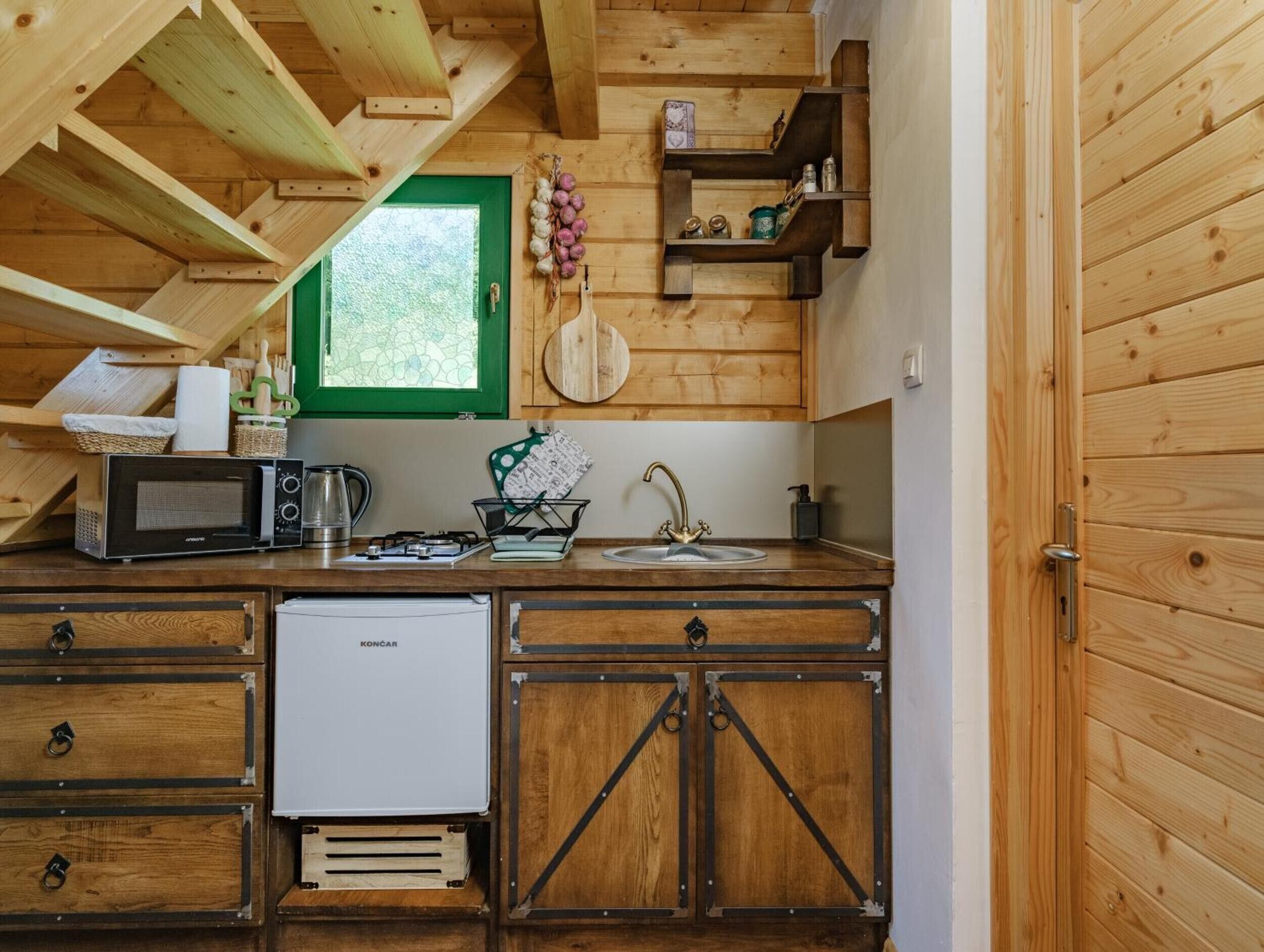 Una cucina compatta con mobili in legno, un forno a microonde, un bollitore e un piccolo frigorifero.