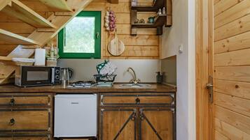 Una cucina compatta con mobili in legno, un forno a microonde, un bollitore e un piccolo frigorifero.