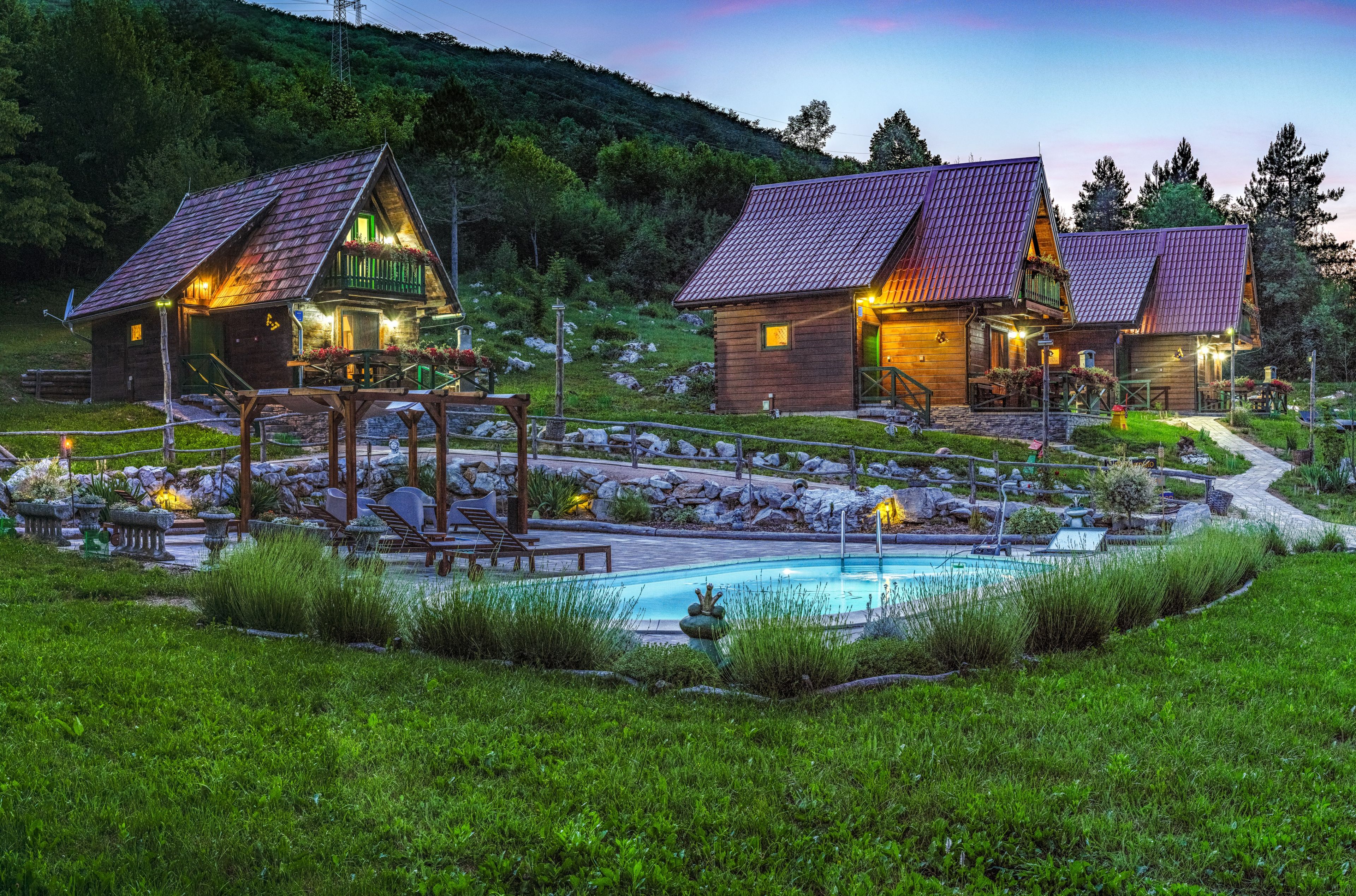 Dos cabañas de madera con tejados de tejas rojas, una piscina y un jardín bien cuidado.