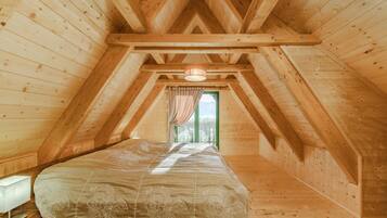 Une chambre avec un plafond en pente, des murs en bois, un lit recouvert d’une couvre-lit à motifs floraux et une fenêtre avec des rideaux.