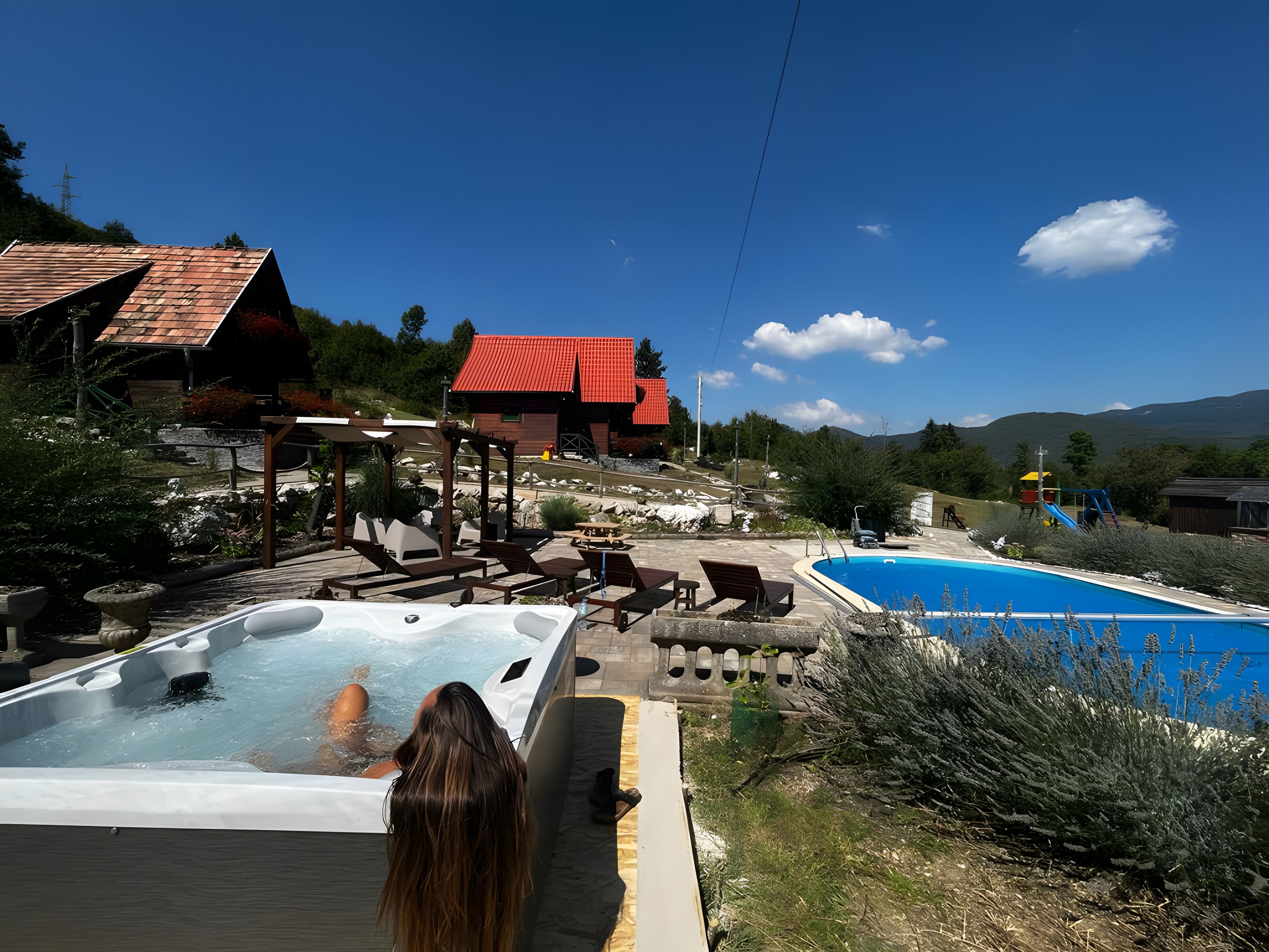 A hot tub area with a pool, outdoor seating, and a view of the surrounding landscape.