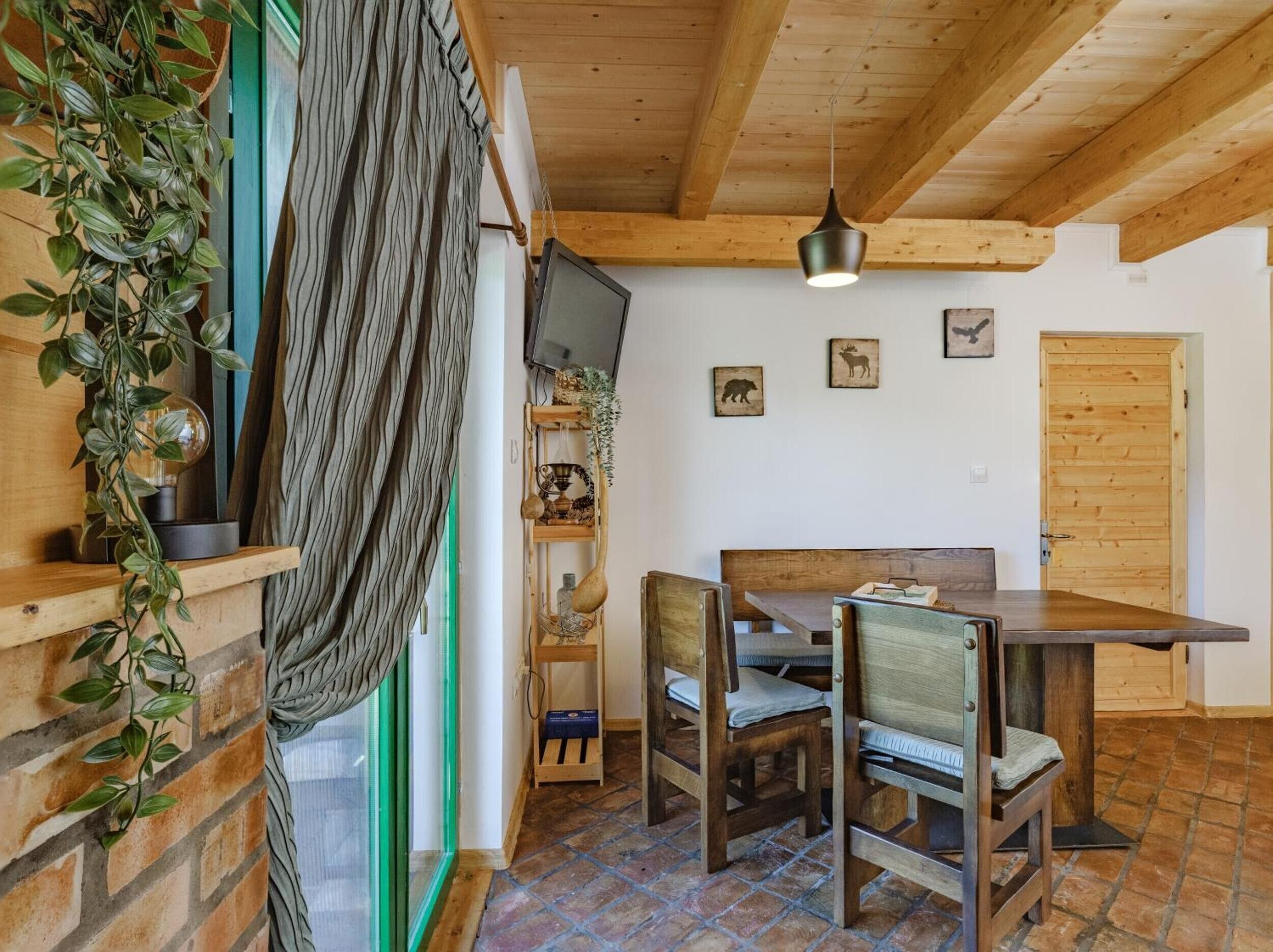 Un comedor con una mesa y sillas de madera, una lámpara colgante y un televisor instalado en la pared.