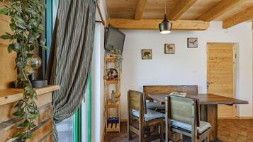 Un comedor con una mesa y sillas de madera, una lámpara colgante y un televisor instalado en la pared.
