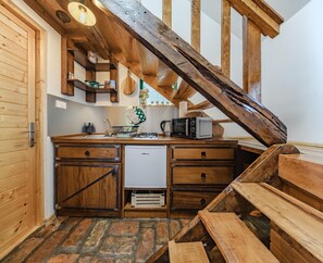 Una cocina rústica con vigas de madera, microondas integrado y un refrigerador pequeño.
