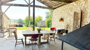 An outdoor patio with a stone wall, a table, chairs, and a grill.