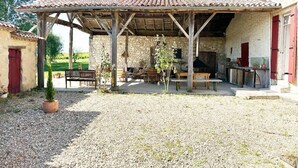 A rustic outdoor seating area with a wooden pergola, stone walls, and a gravel ground.
