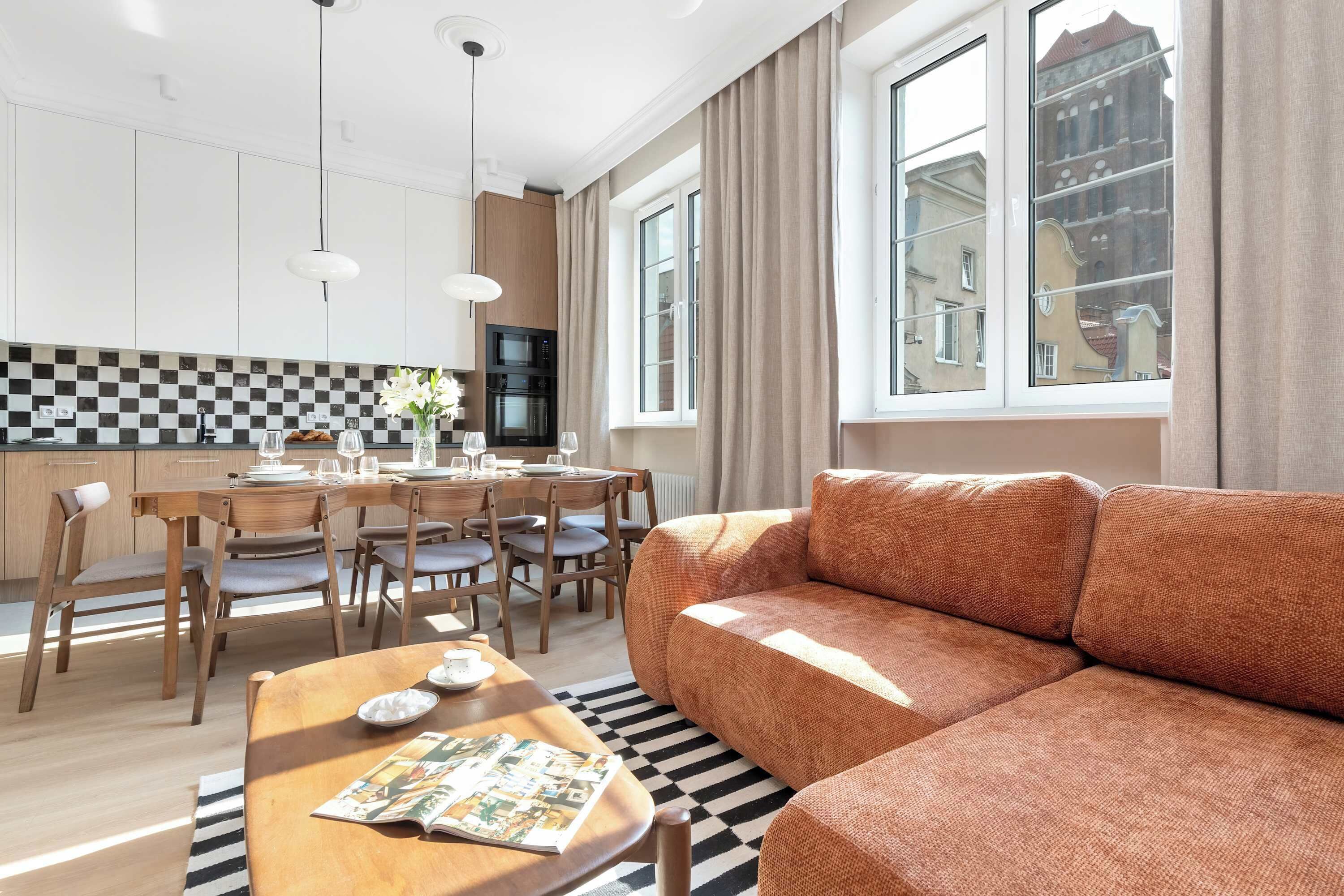 Una sala de estar moderna con un sofá, una mesa de comedor para cuatro personas y una cocina equipada con microondas y horno.