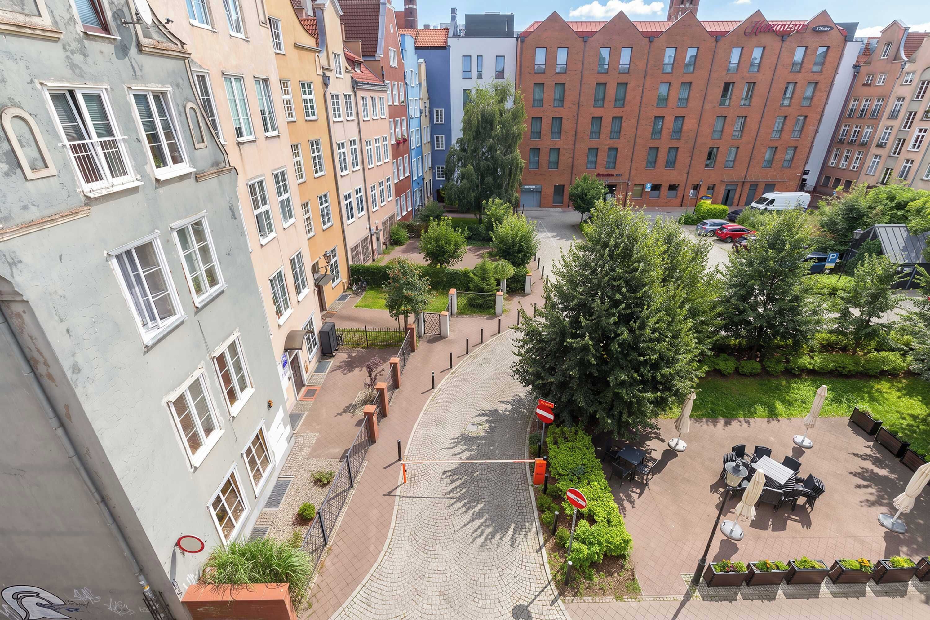 A courtyard with a cobblestone path, surrounded by multi-story buildings with various architectural styles.