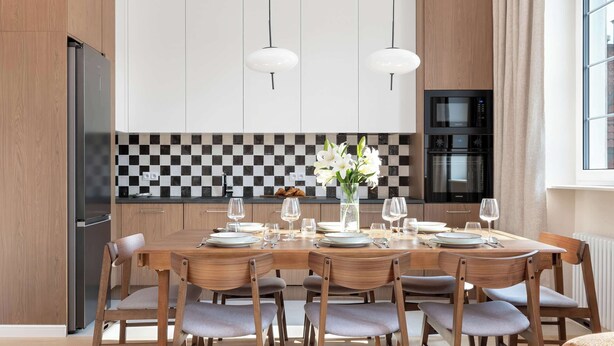 Une cuisine moderne avec une table à manger pour six personnes, des chaises en bois, un réfrigérateur noir, un four à micro-ondes et un pare-feu à carreaux.