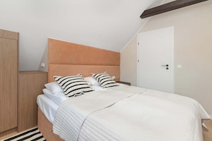 A bedroom with a bed, two pillows, a wooden wardrobe, and a white door. - Sedan Apartments  Gdansk by Noclegi Renters (Gdańsk)