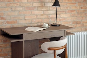 A wooden desk with a book, a cup, and a lamp against a brick wall. - Sedan Apartments  Gdansk by Noclegi Renters (Gdańsk)