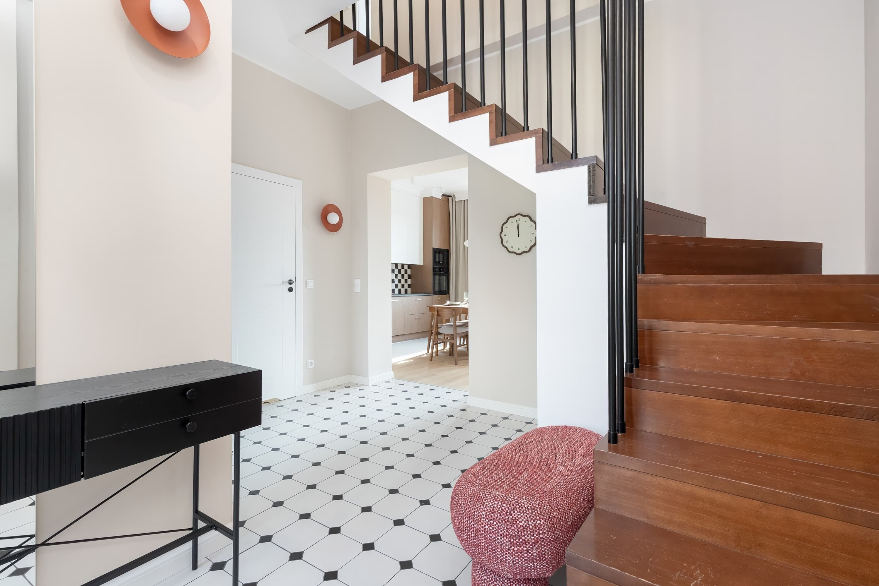 A modern interior with a staircase, a dining area, and a kitchen visible through an open door.