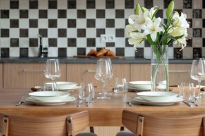 Una mesa de comedor puesta con platos, cubiertos y copas de vino, con un florero de flores blancas en el centro.