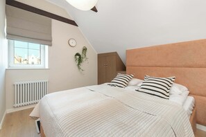 A bedroom with a bed, a window, a radiator, a clock, and a plant. - Sedan Apartments  Gdansk by Noclegi Renters (Gdańsk)