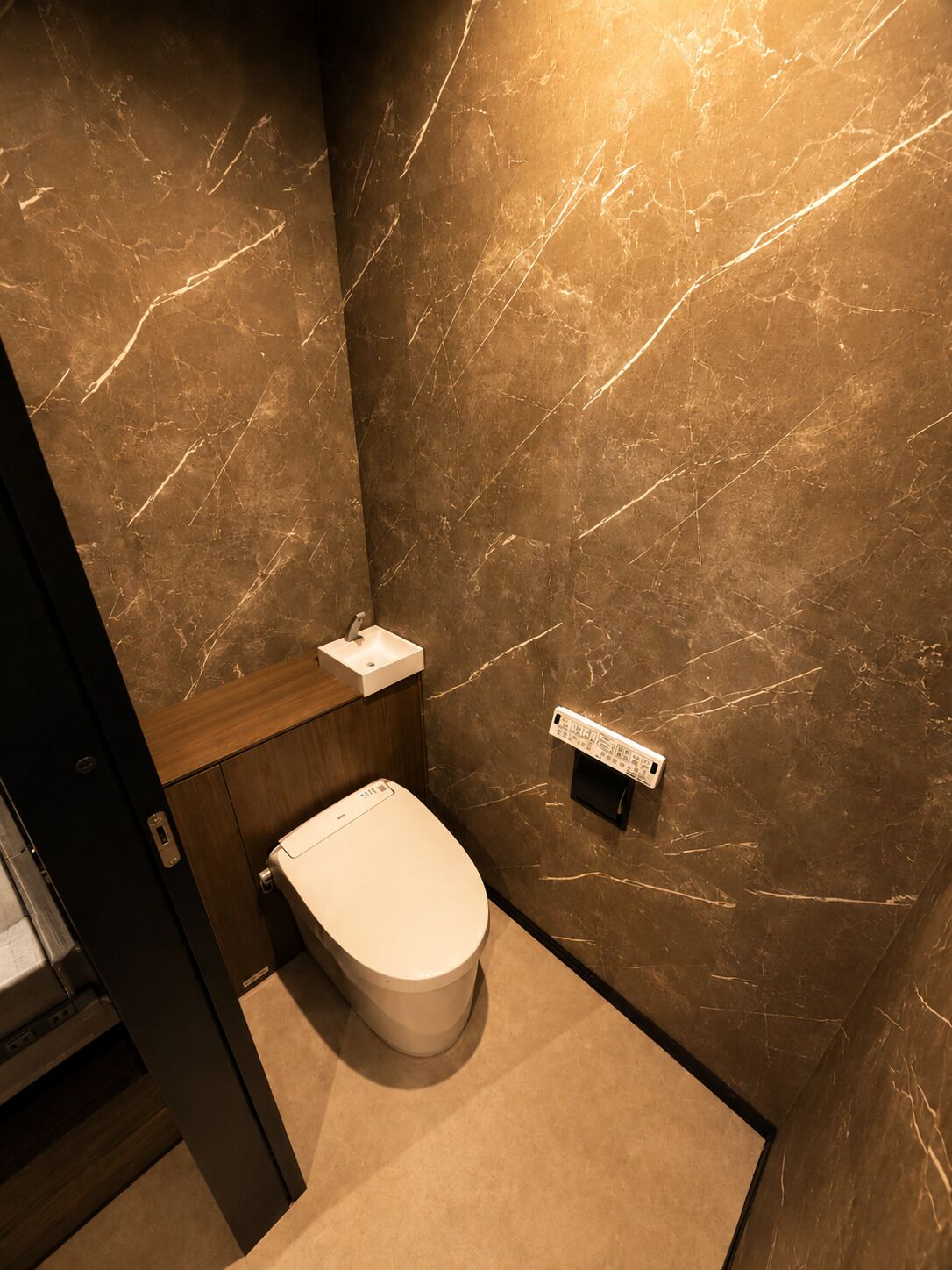A modern bathroom with a marble wall, a toilet, and a small sink.