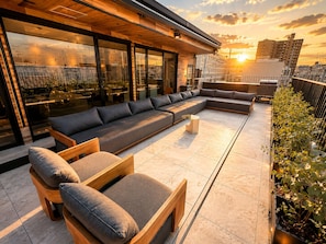 En takterrass med modern design, inredd med en lång soffa, trästolar och ett glasräcke.