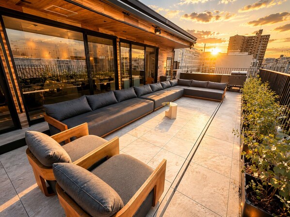 Eine Dachterrasse mit modernem Design, mit einer langen Sitzecke, Holzstühlen und einer Glasumlaufung.