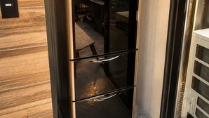 A HITACHI refrigerator in a corner of a room with a wooden floor and a view of a cityscape through a glass door. - Flam Hotel Luxury Penthouse Osaka | Sauna & Rooftop Terrace Near USJ (大阪市)
