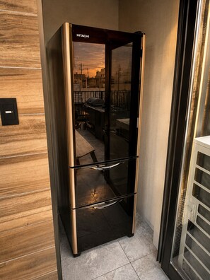 A HITACHI refrigerator in a corner of a room with a wooden floor and a view of a cityscape through a glass door. - Flam Hotel Luxury Penthouse Osaka | Sauna & Rooftop Terrace Near USJ (大阪市)