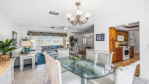 A modern living room with a glass dining table, a ceiling fan, and a kitchen area with wooden cabinets. - 3 Bedroom/3.5 bath waterfront pool home with dock and lift (Marco Island)