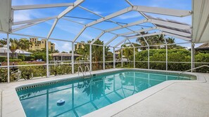 A swimming pool with a glass enclosure, surrounded by greenery and buildings in the background. - 3 Bedroom/3.5 bath waterfront pool home with dock and lift (Marco Island)