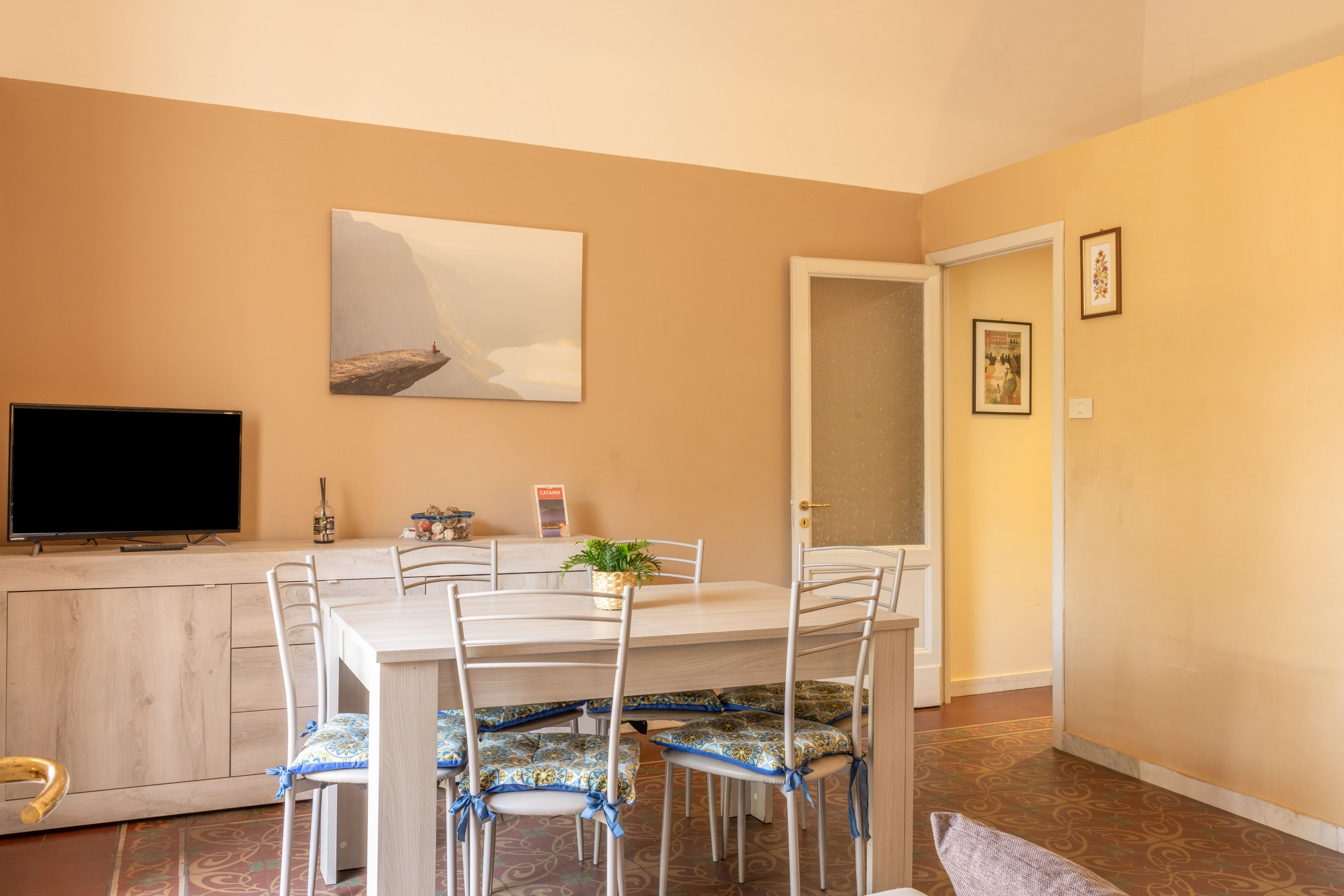 A dining area with a table, chairs, a television, and a painting on the wall.
