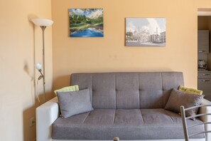 Un canapé gris avec deux coussins, un lampadaire et deux tableaux accrochés au mur.