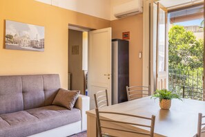 Un salon avec un canapé, une table à manger et des chaises, une plante en pot et une vue sur l’extérieur.